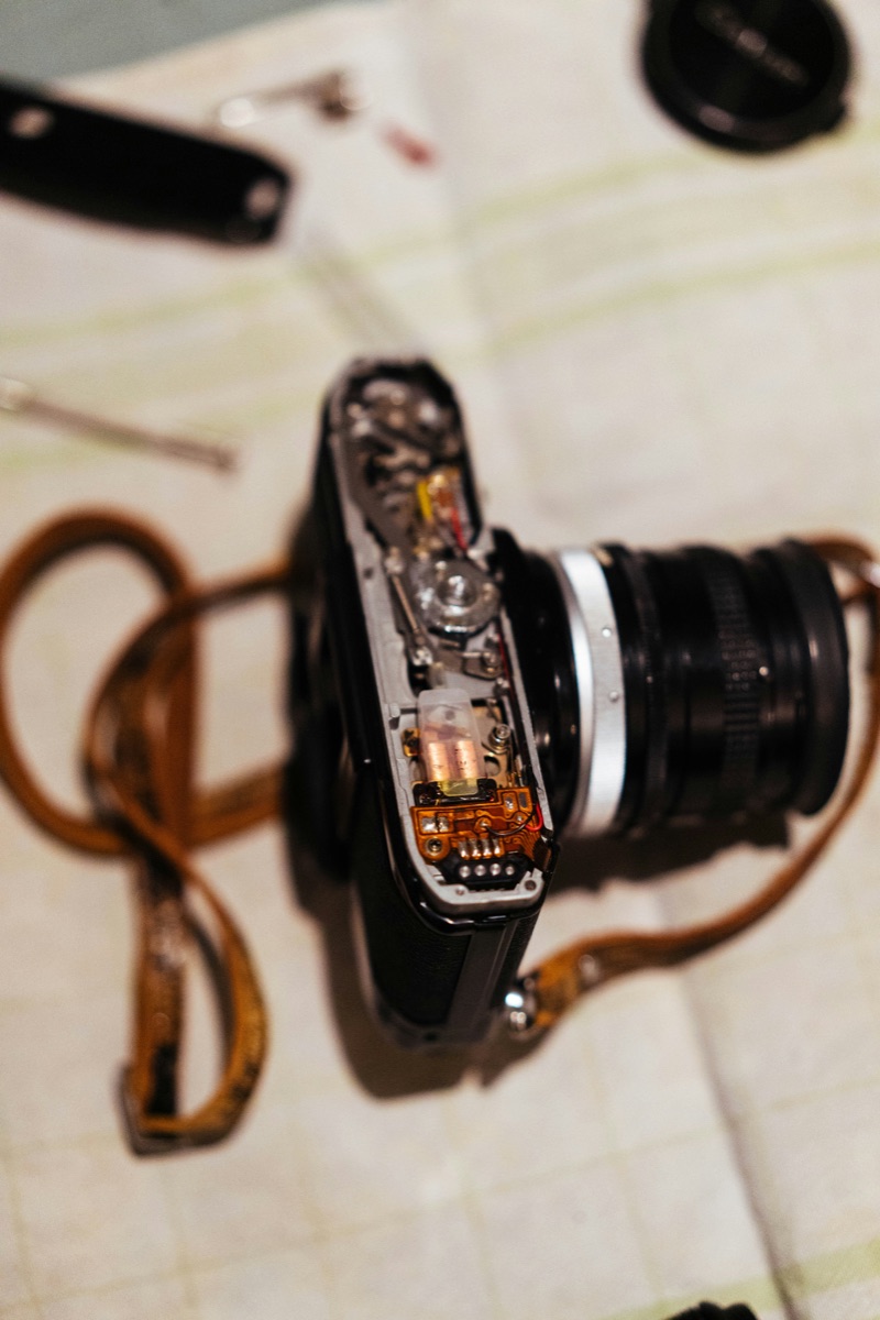 A disassembled camera with internal components, tools, and a camera strap laid out on a table during a repair