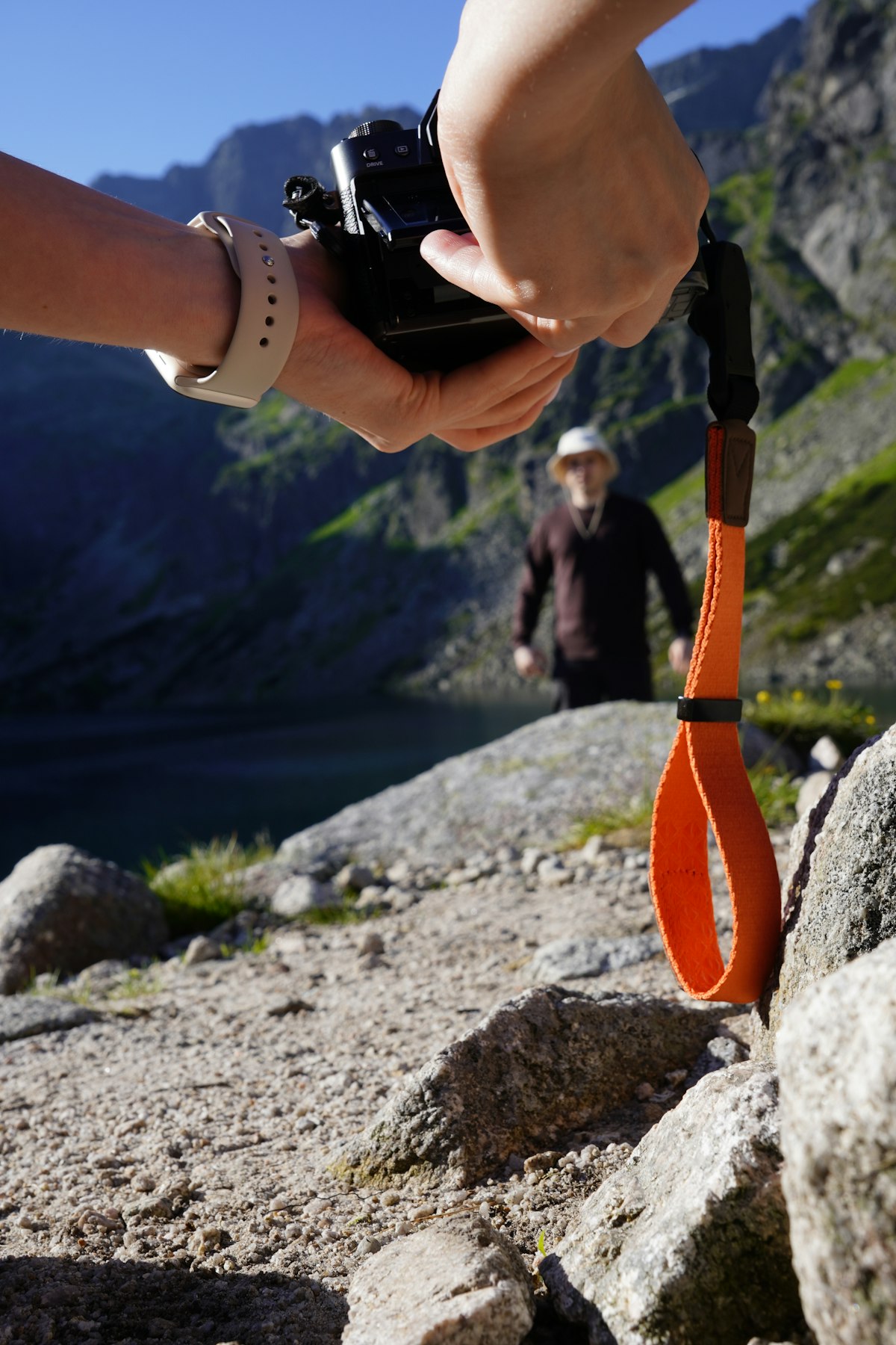 Hands holding a camera secured by a wrist strap in the mountains