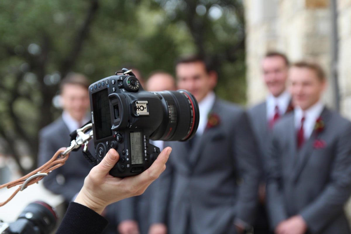 A wedding photographer holding up a DSLR camera to photograph groomsmen