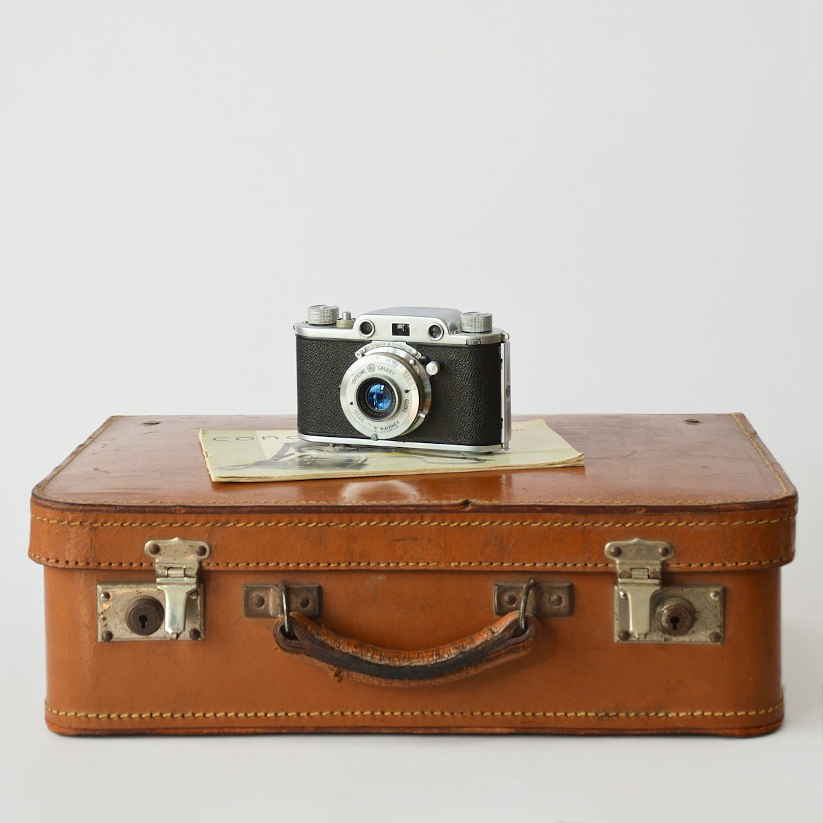 A vintage camera resting on top of a vintage leather suitcase