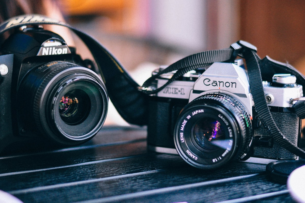 A Nikon DSLR and a Canon AE-1 film camera side by side on a wooden table