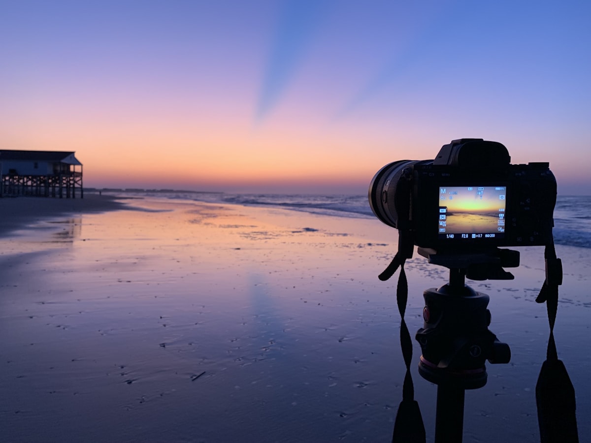A camera on a tripod facing the ocean at the shoreline during sunset